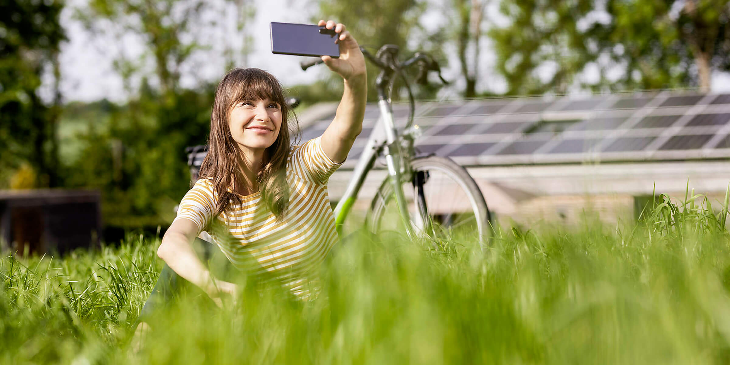 Eine Frau mit Fahrrad macht ein Selfie vor ihrer Photovoltaikanlage.