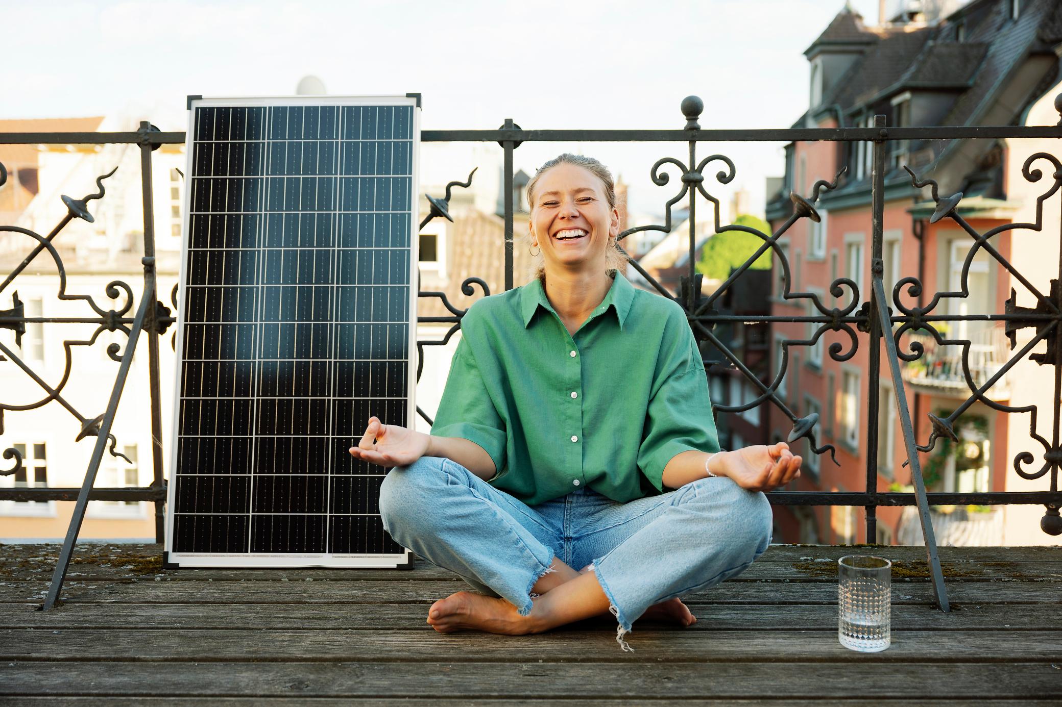 Frau macht Yoga auf dem Balkon und neben ihr steht ein Solarmodul