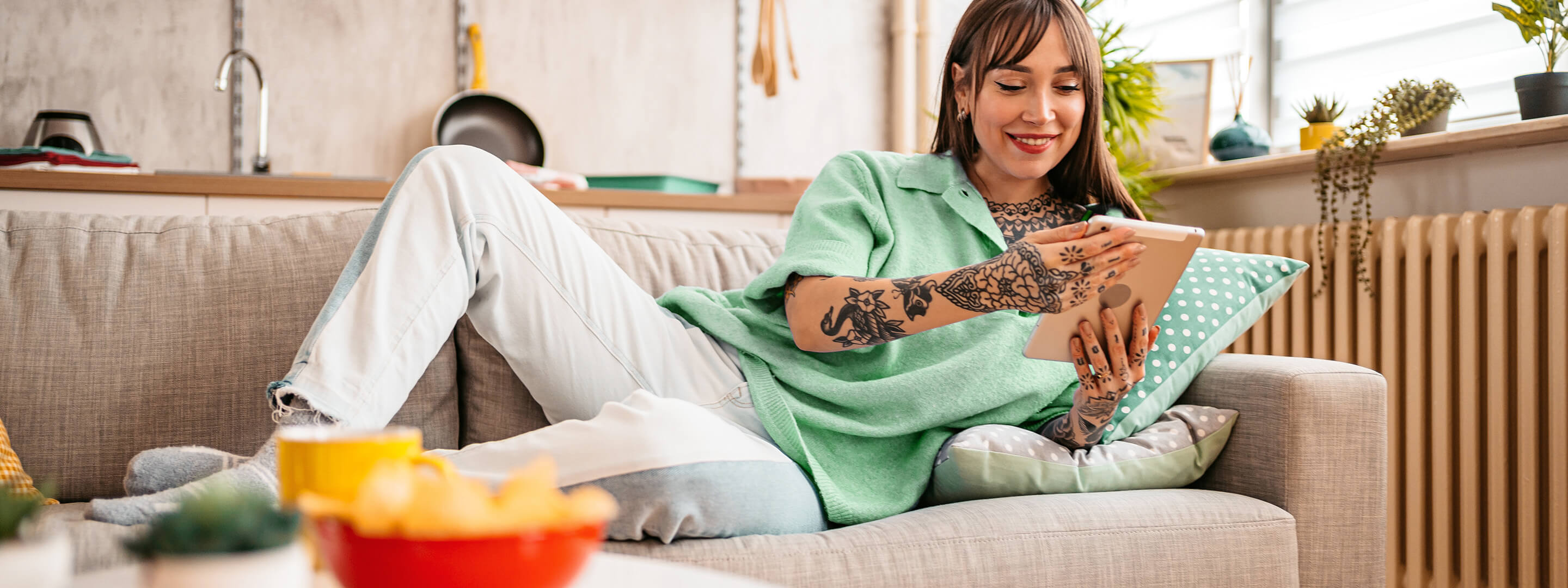 Junge Frau auf dem Sofa steuert mit dem Tablet ihre Smart-Home-Geräte