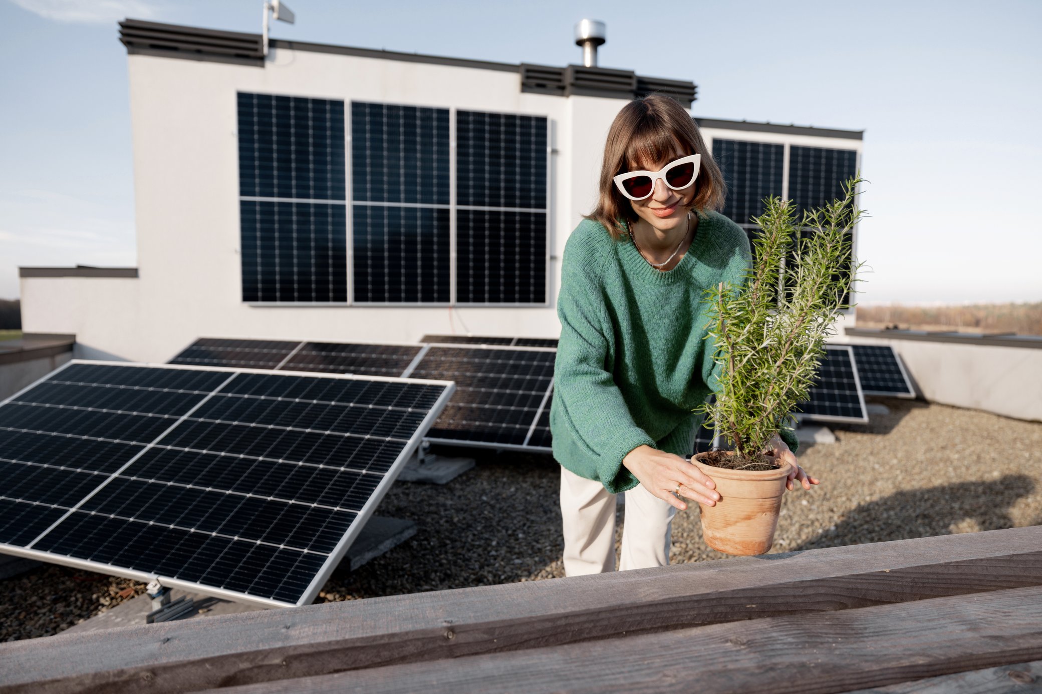 Frau mit Sonnenbrille setzt eine Pflanze auf eine Dachterrasse mit Solarmodulen