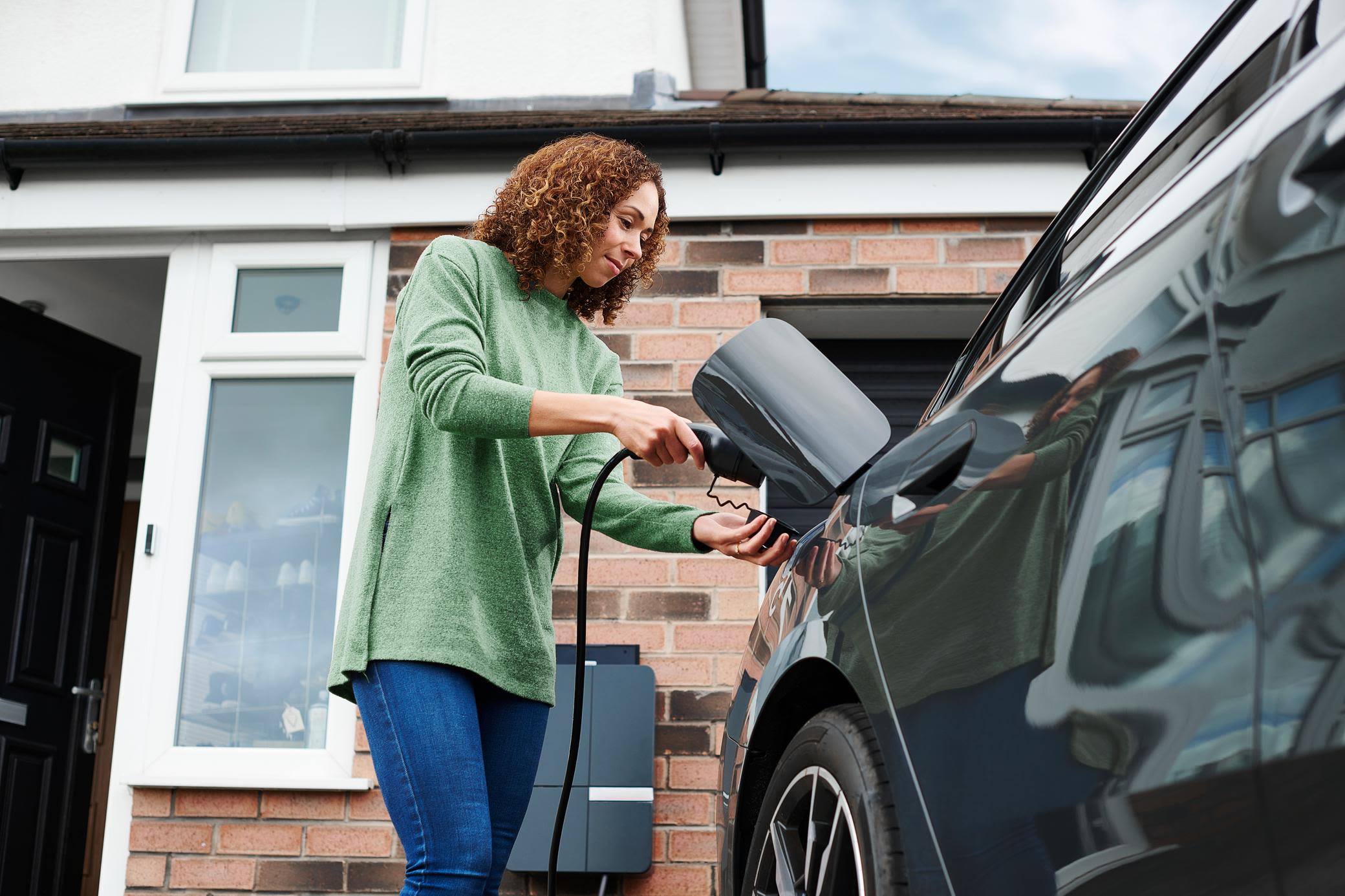 Wallbox mit Solarenergie: So lädst du noch klimafreundlicher auf. Frau im grünen Pullover lädt ihr e-Auto zuhause auf