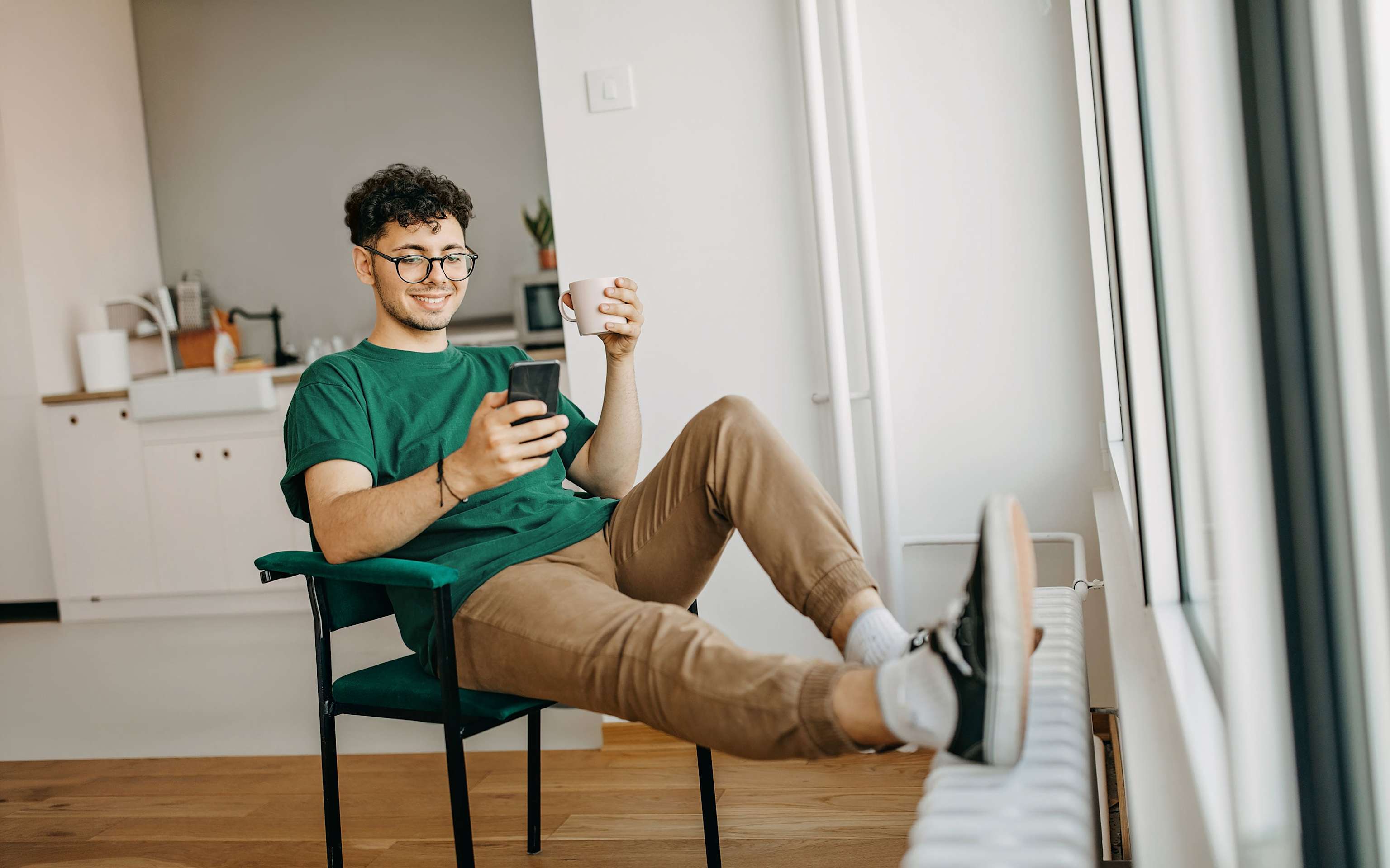 Mann schaut auf sein Handy und legt die Füße auf die Heizung Mann schaut auf sein Handy und legt die Füße auf die Heizung