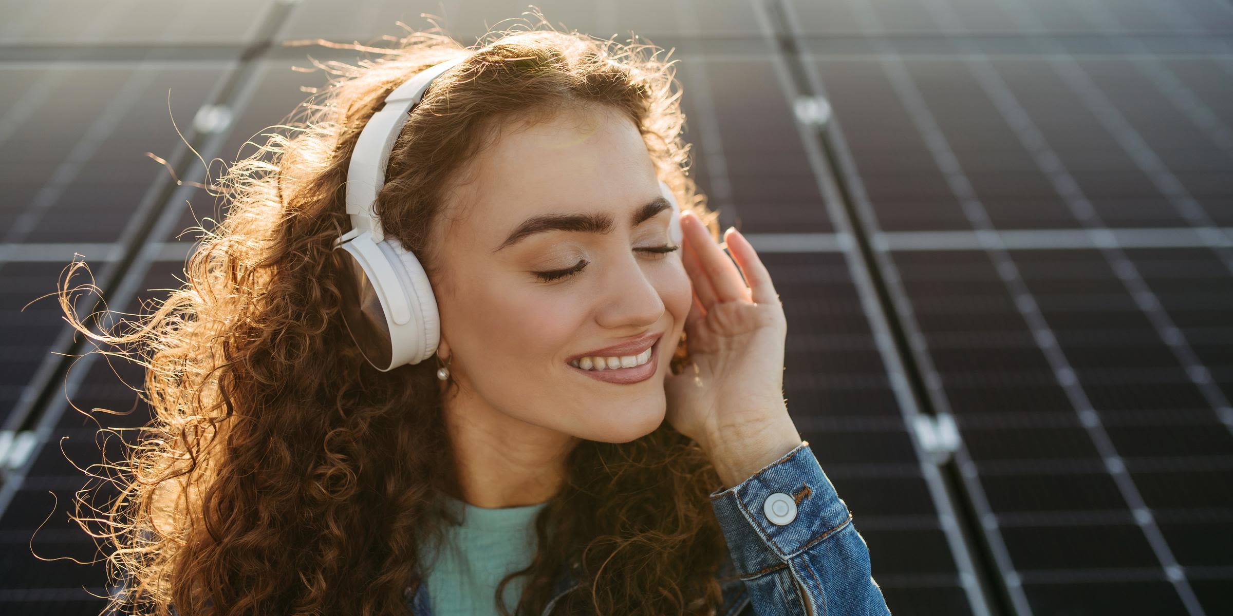 Mit einer Solaranlage holst du dir gute Energie nach Hause Frau mit Kopfhörern hört Musik vor Solaranlage
