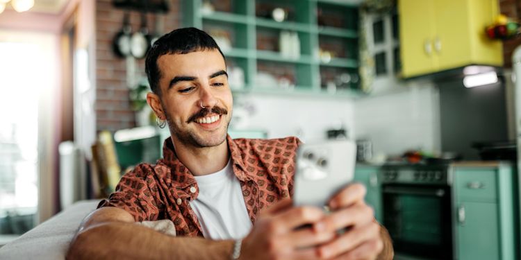 Infos zur Smart-Meter-Pflicht in Deutschland auf einen Blick Lächelnder Mann sitzt auf dem Sofa und checkt auf dem Smartphone seinen Energieverbrauch