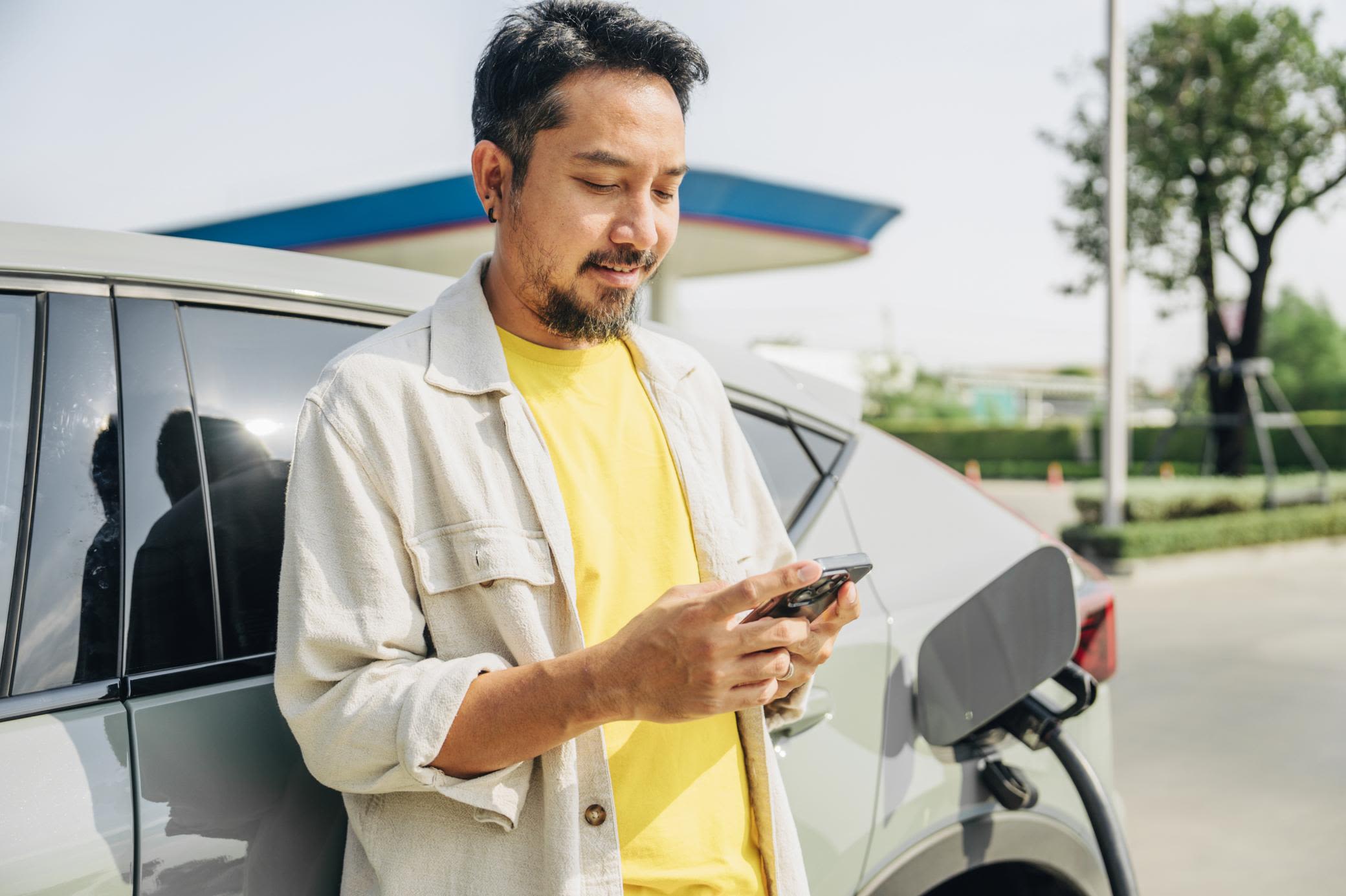Unterwegs das E-Auto laden geht schnell und komfortabel Ein Mann im gelben T-Shirt lädt sein E-Auto unterwegs und schaut aufs Handy