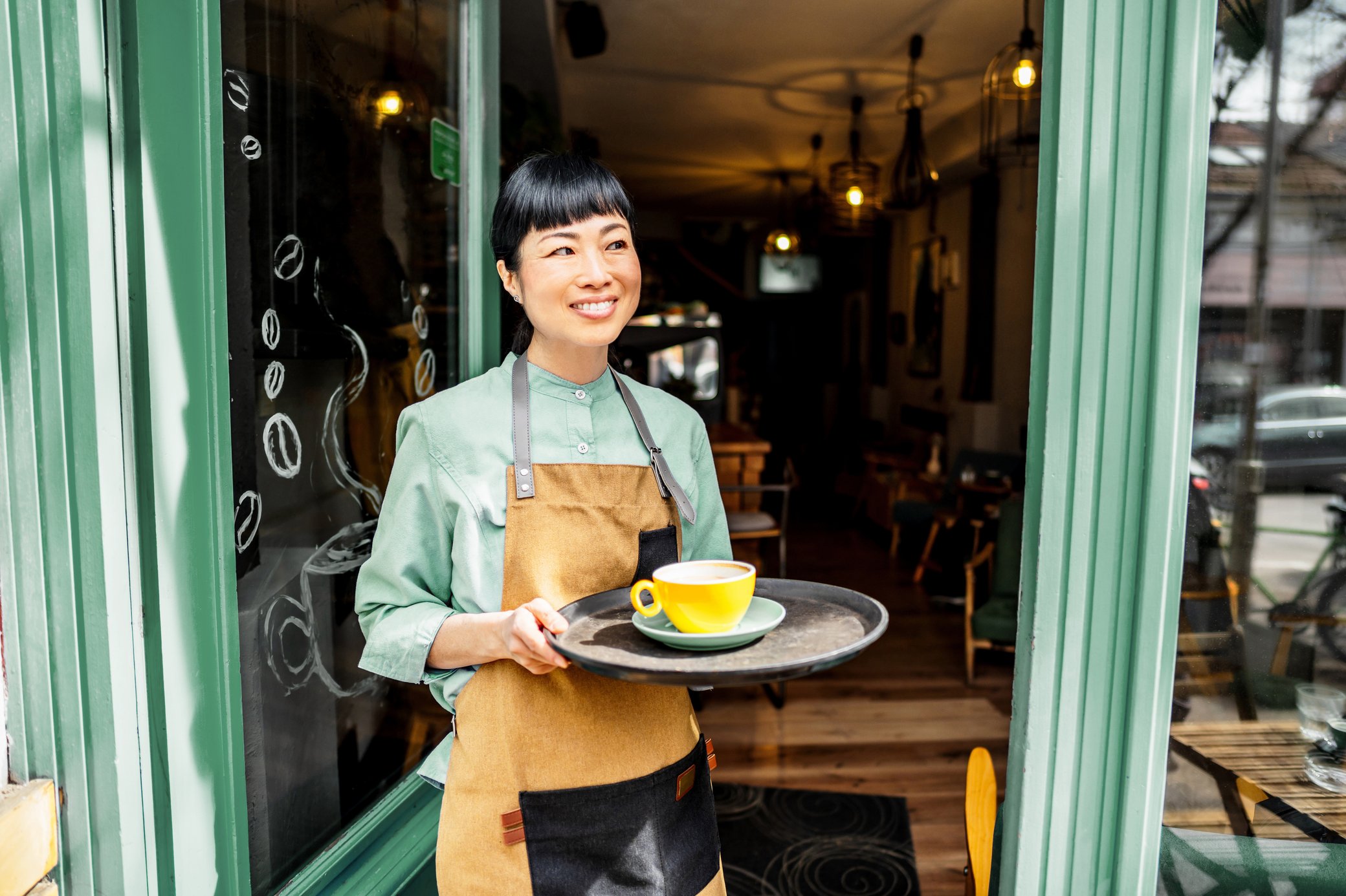 Frau vor einem Cafe mit Tablett und gelber Kaffeetasse