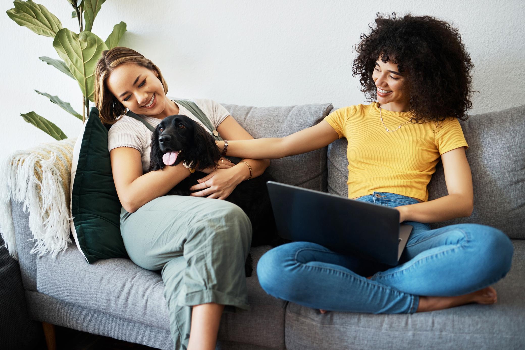 Zwei Frauen sitzen mit Hund und Laptop auf der Couch