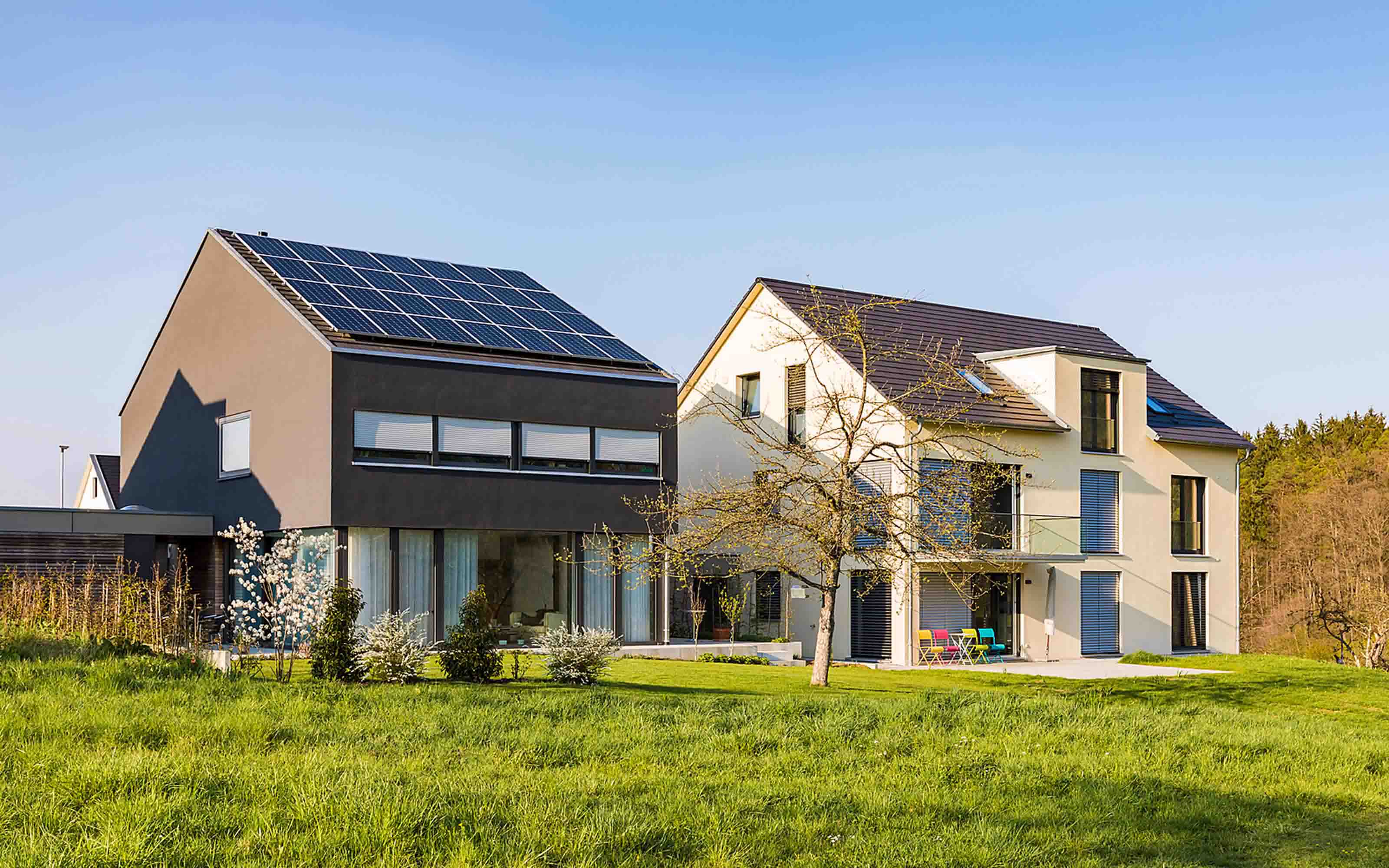 Modernes Einfamilienhaus mit Photovoltaik-Anlage steht neben Haus ohne Photovoltaik-Anlage