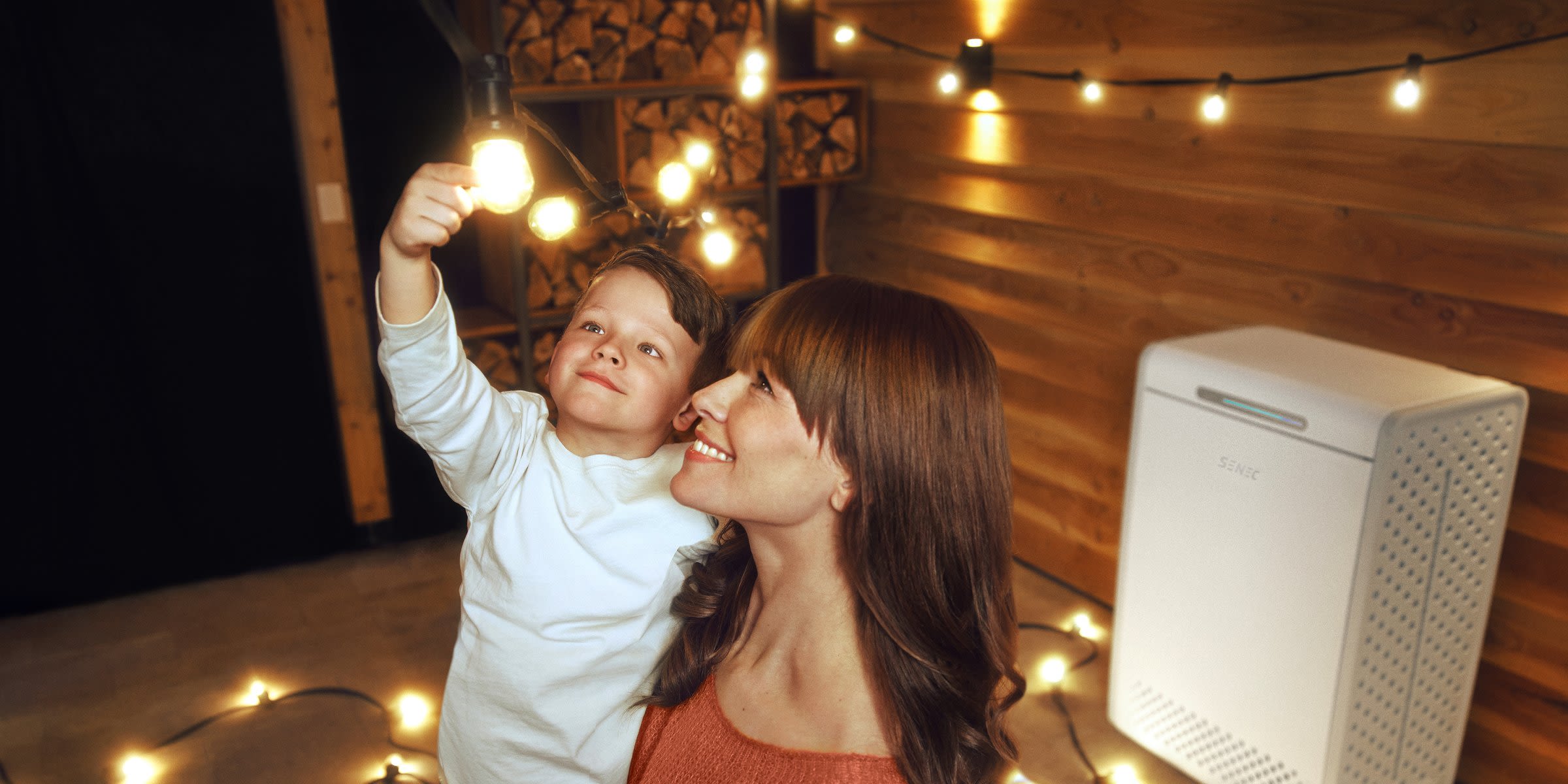Einen Heimspeicher kannst du auch ohne Solaranlage nutzen Eine Mutter hält ihren kleinen Sohn auf dem Arm vor einem Heimspeicher