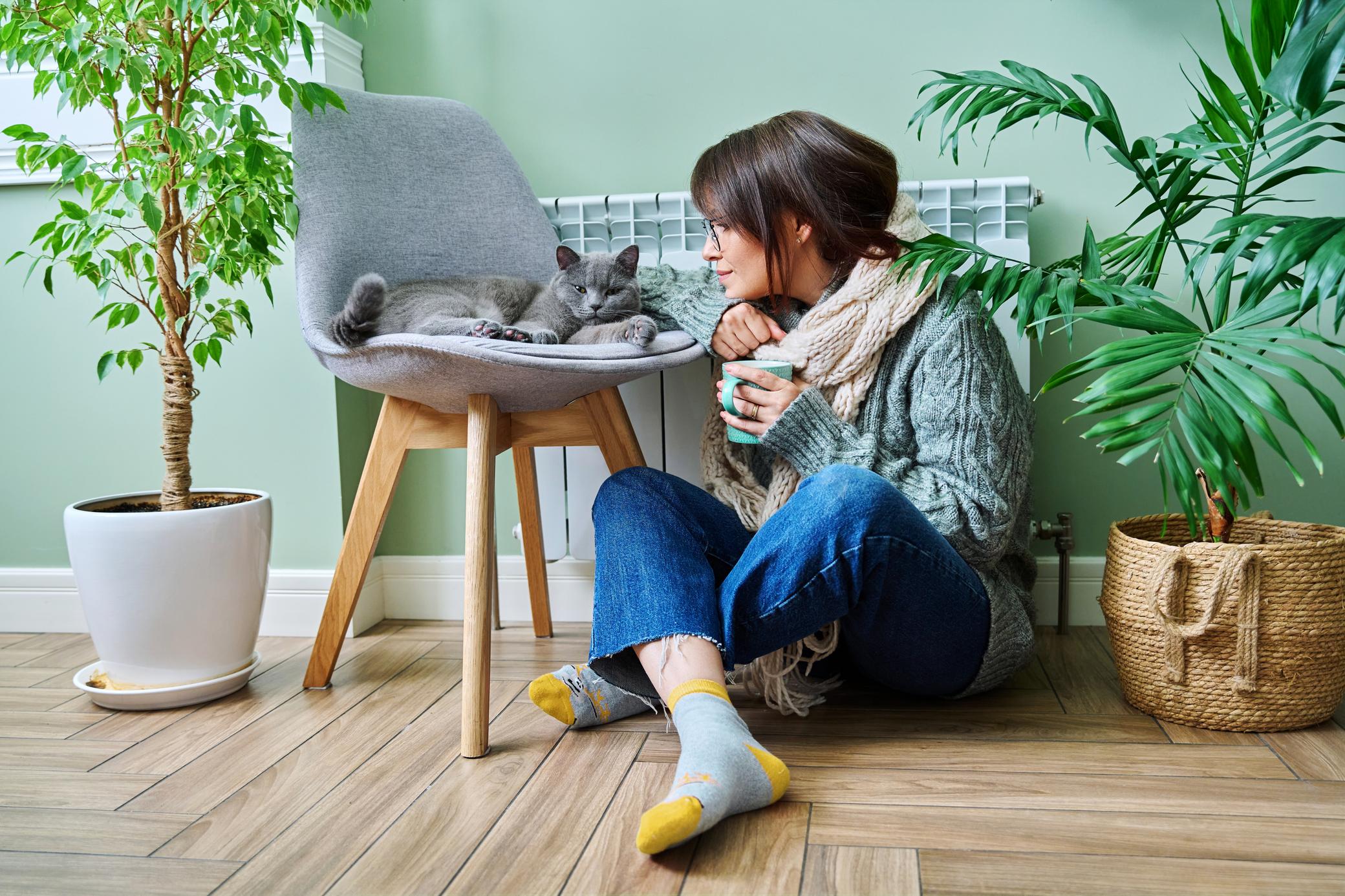 Frau sitzt in warmer Kleidung mit Katze vor der Heizung