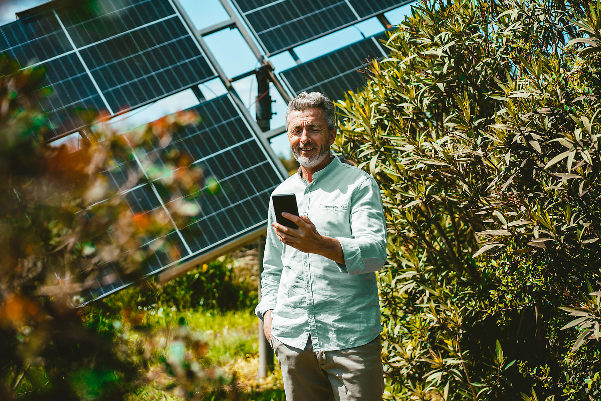 Mit einer Solaranlage tust du Umwelt und Konto etwas Gutes Mann steht mit dem Handy vor einer Solaranlage im Grünen