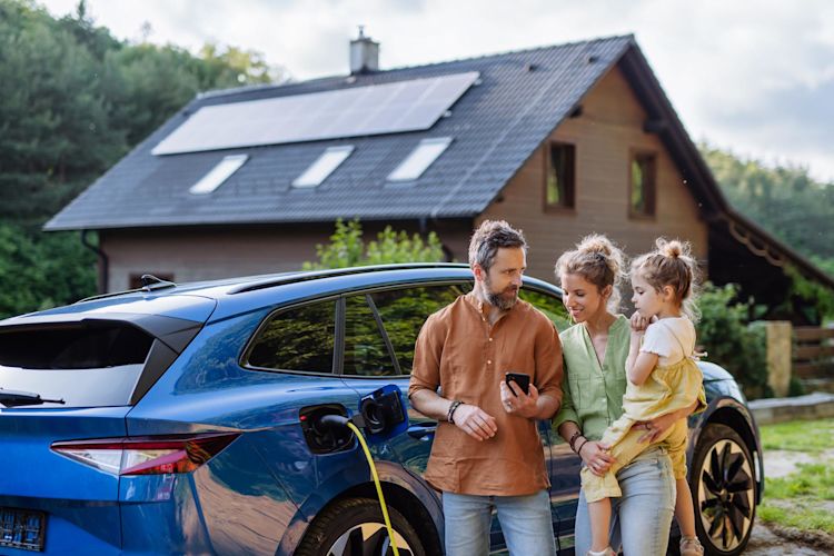 Ob Volleinspeisung oder Eigenbedarf - mit Solar auf dem Dach hat man viele Vorteile und Möglichkeiten. Familie mit Mädchen laden Elektroauto vor dem Haus mit Solaranlage auf dem Dach