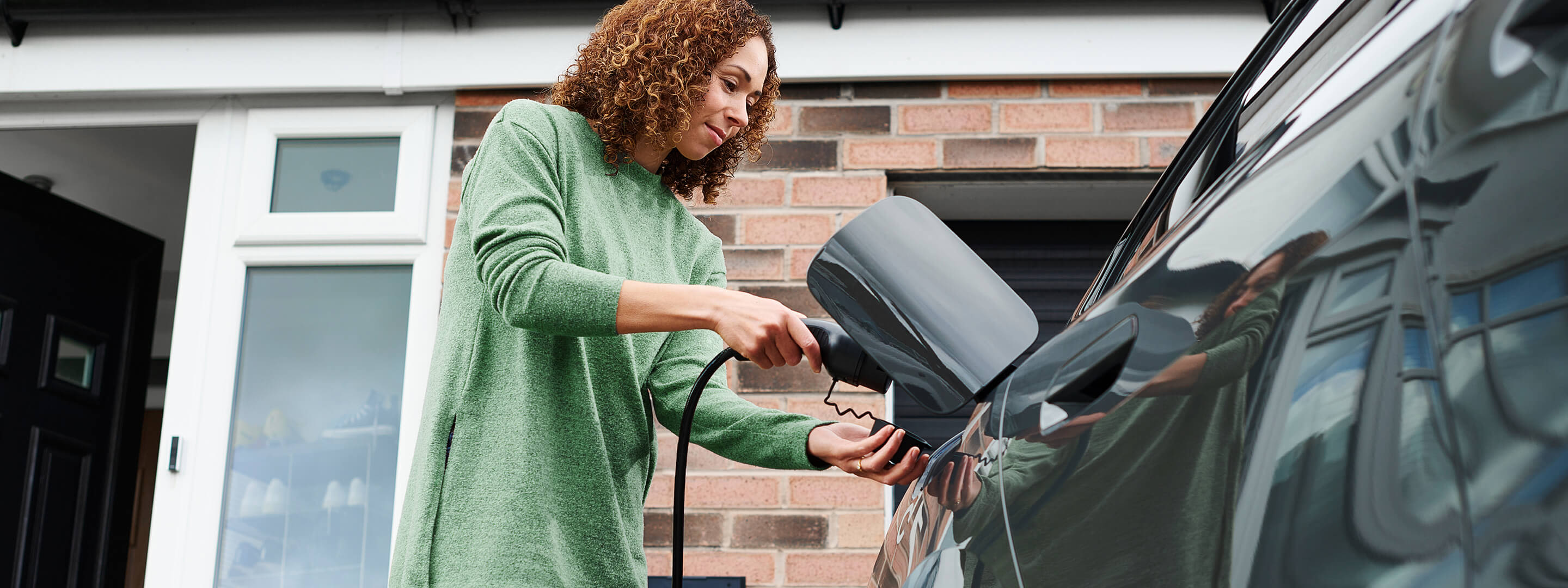 Mit einer Wallbox Förderung günstig zuhause laden Frau hängt das Ladekabel für E-Auto über die Wallbox
