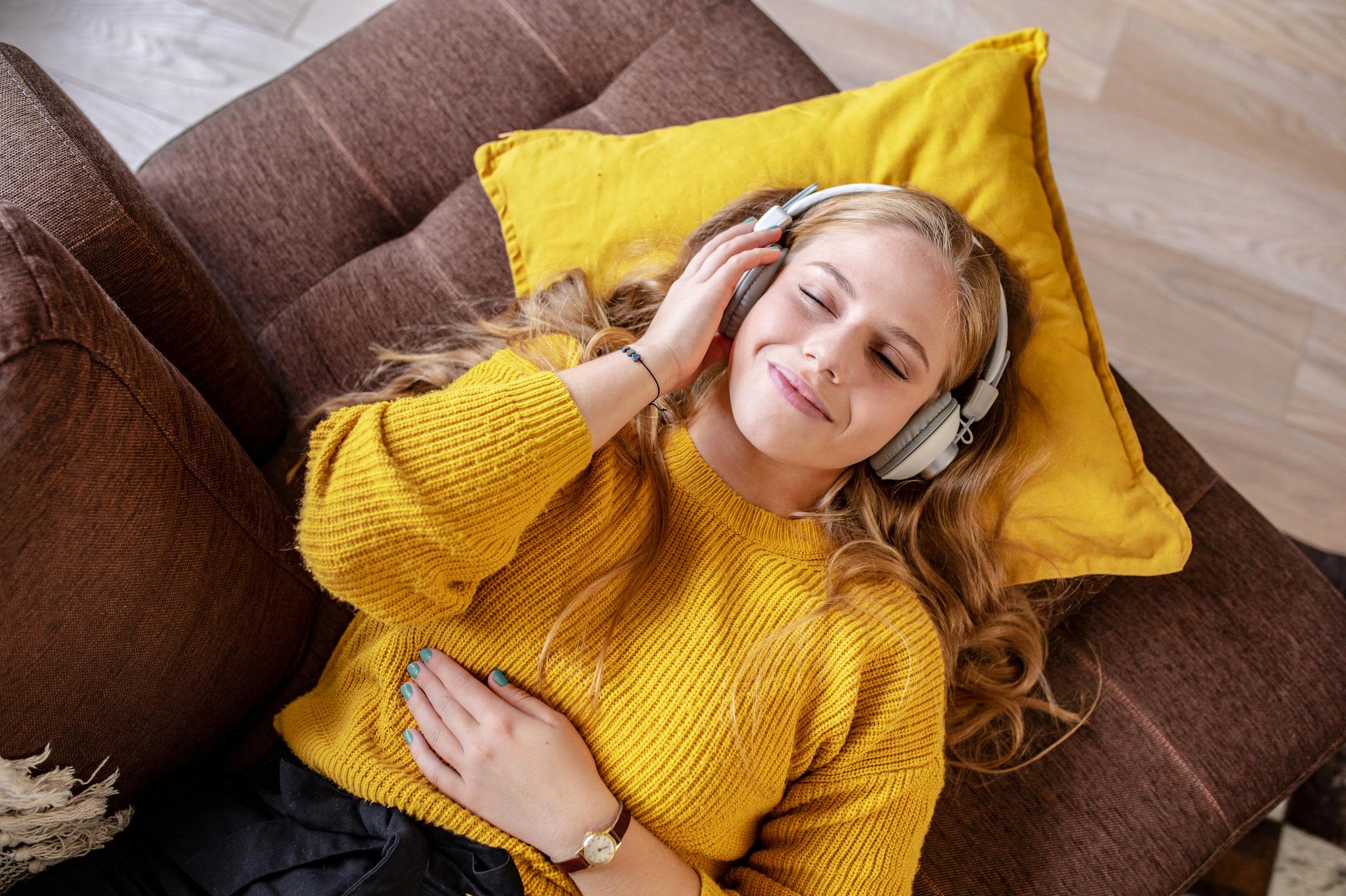 Entspannt dankt richtiger Jahresrechnung: Hast deine Energiepreisbremse überprüft? Junge Frau entspannt auf Sofa und hört Musik