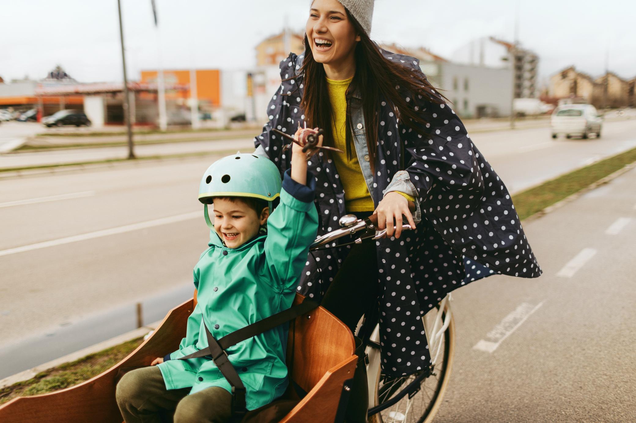 Fröhliche Frau mit Lastenfahrrad und Kind in der Stadt