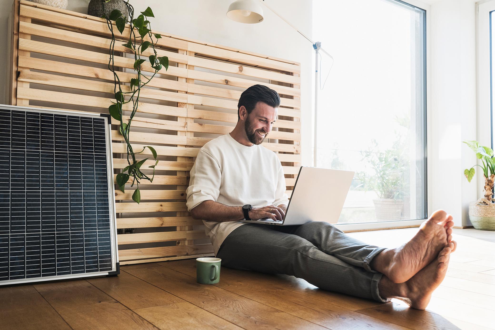 Mann der neben einem Solarmodul sitzt und einen Laptop benutzt