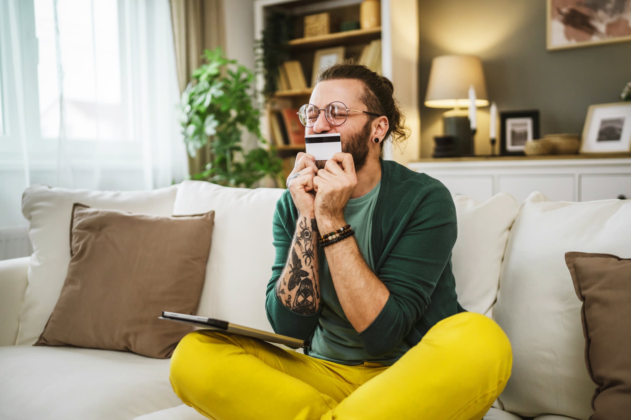 Bei deinen Energiekosten sparen? Es gibt immer Möglichkeiten, Foto von einem jungen Mann, der auf dem Sofa sitzt und seine Kreditkarte küsst